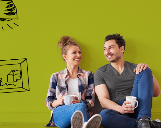 Smiling couple with coffee mugs sitting on the floor against a green wall