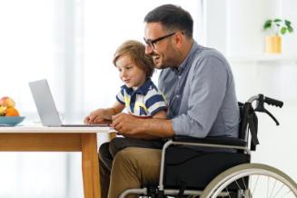 Man in wheelchair looks at laptop computer with his young son