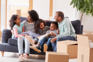 Happy family of 5 sitting on couch surrounded by moving boxes